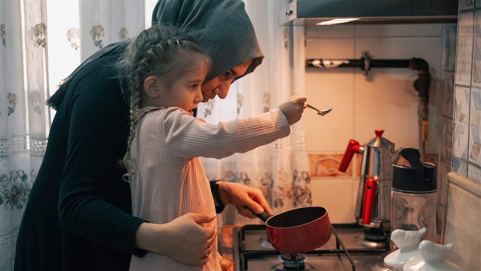 A parent and child cooking together in a busy home kitchen