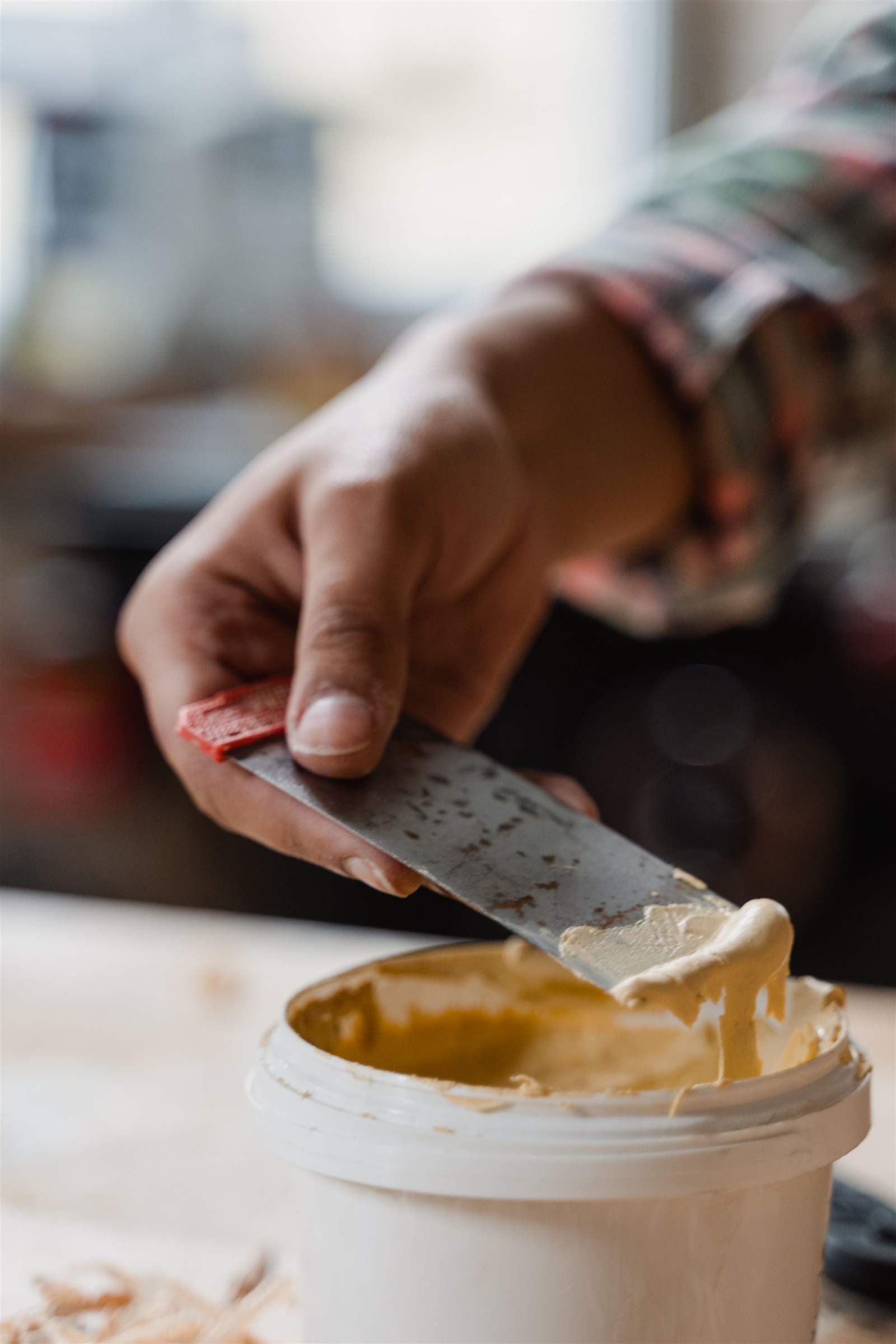 Craftsman's hand applying wood filler to a wooden surface with a putty knife