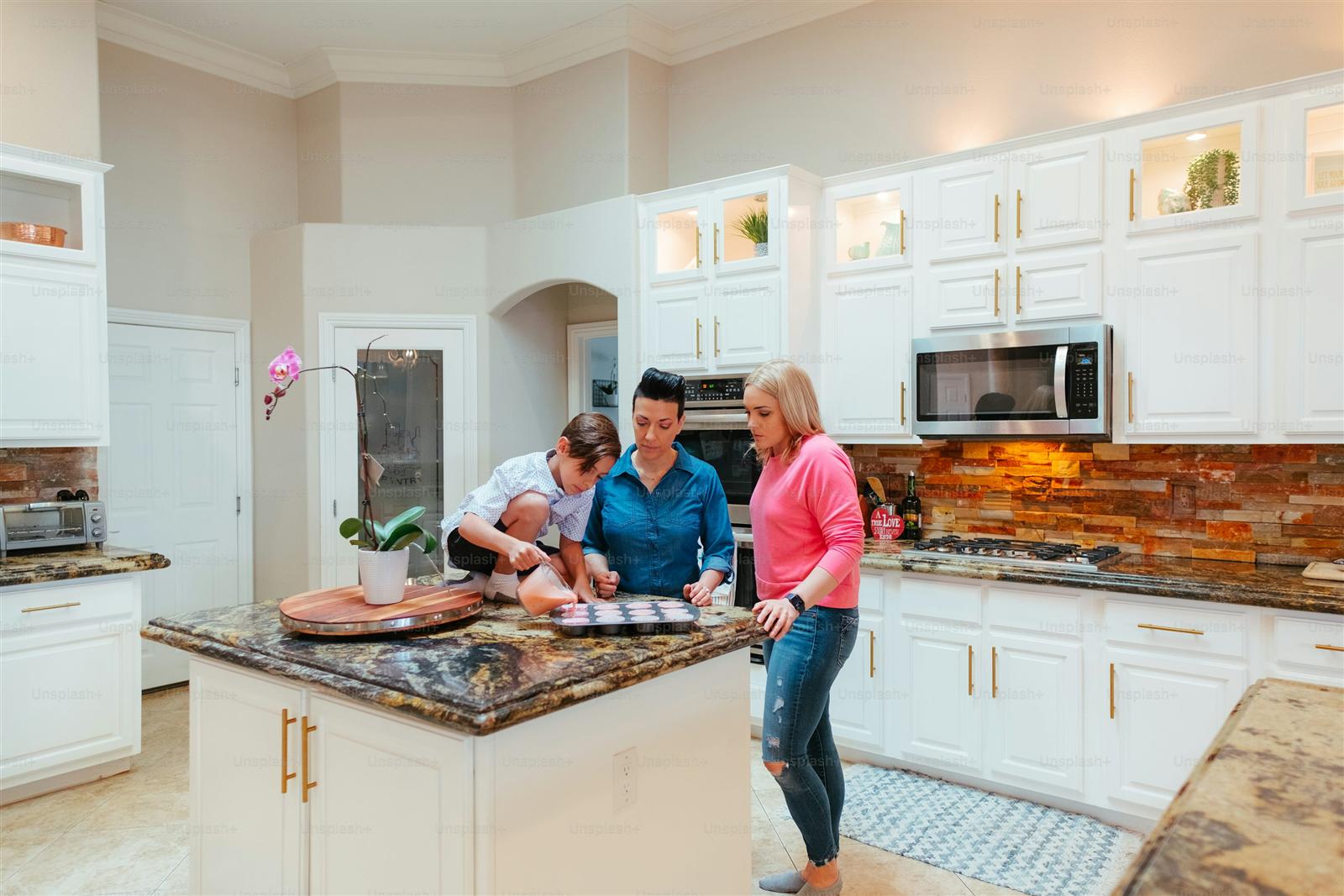 A group of people gathered around a bright kitchen island, illustrating why an island is worth adding for entertaining and connection